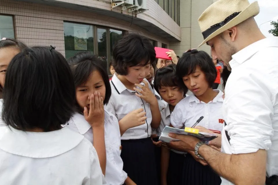 Schoolgirls in white uniforms gather around Christian Muñoz as he writes in a notebook outside a building in Pyongyang.