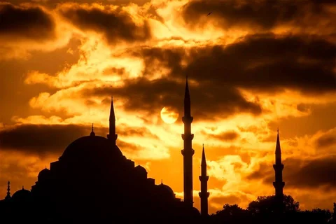 Silhouetted mosque and minarets beneath an orange sunset sky in Istanbul.
