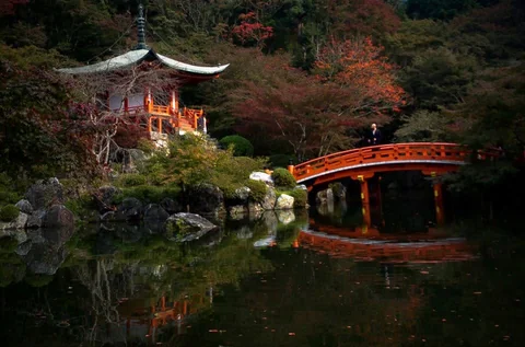 Red bridge, garden, and pavilion beside a pond in Kyoto.