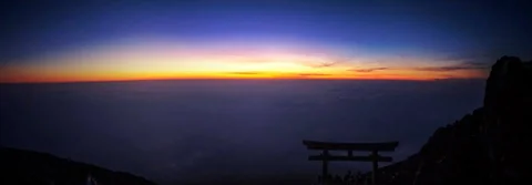 Sunset above clouds with a torii gate silhouetted on Mount Fuji.